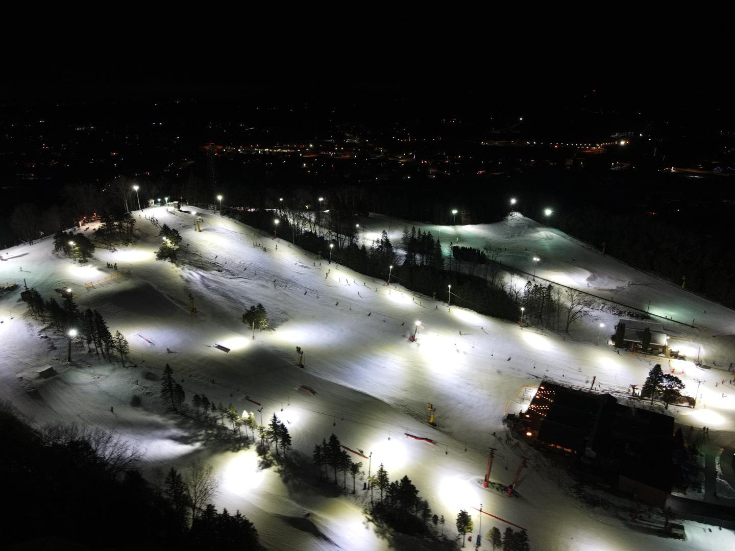 Floodlit ski slopes and lodges at night, viewed from above.