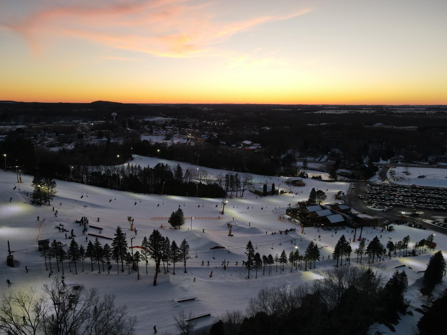 Snow-covered landscape with scattered trees at sunset.