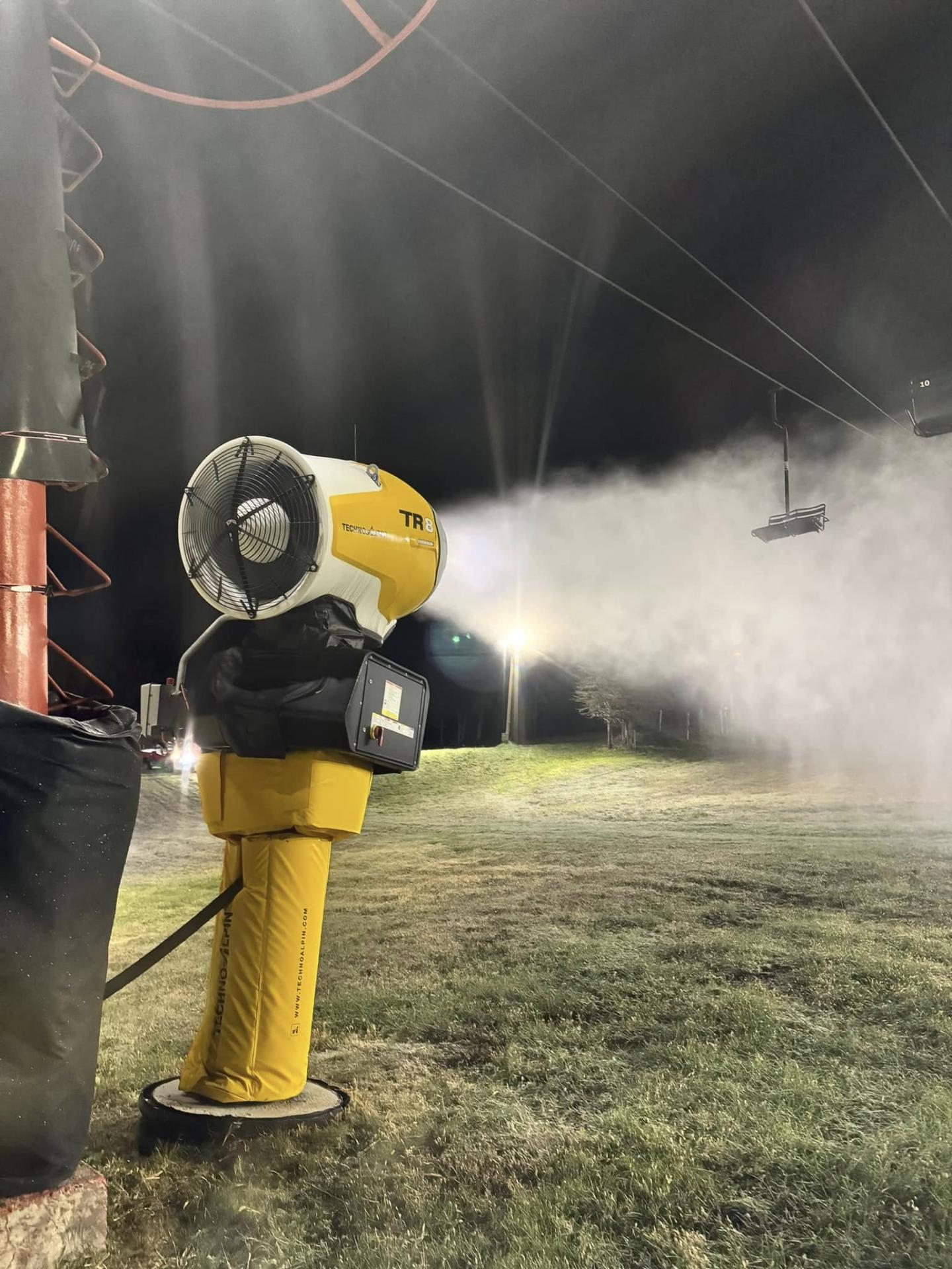 Yellow fire hydrant spraying water across a grassy field at night.