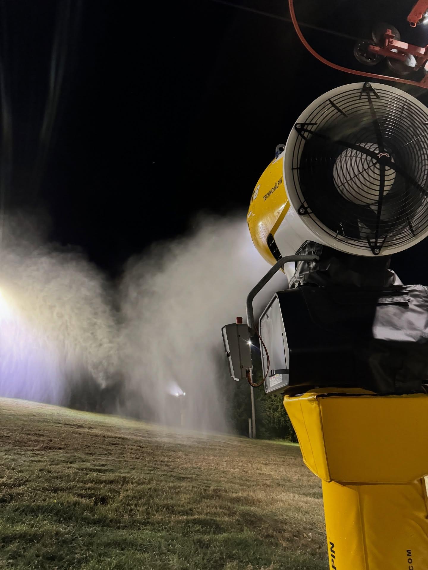 Worker in protective gear spraying mist across a field at night