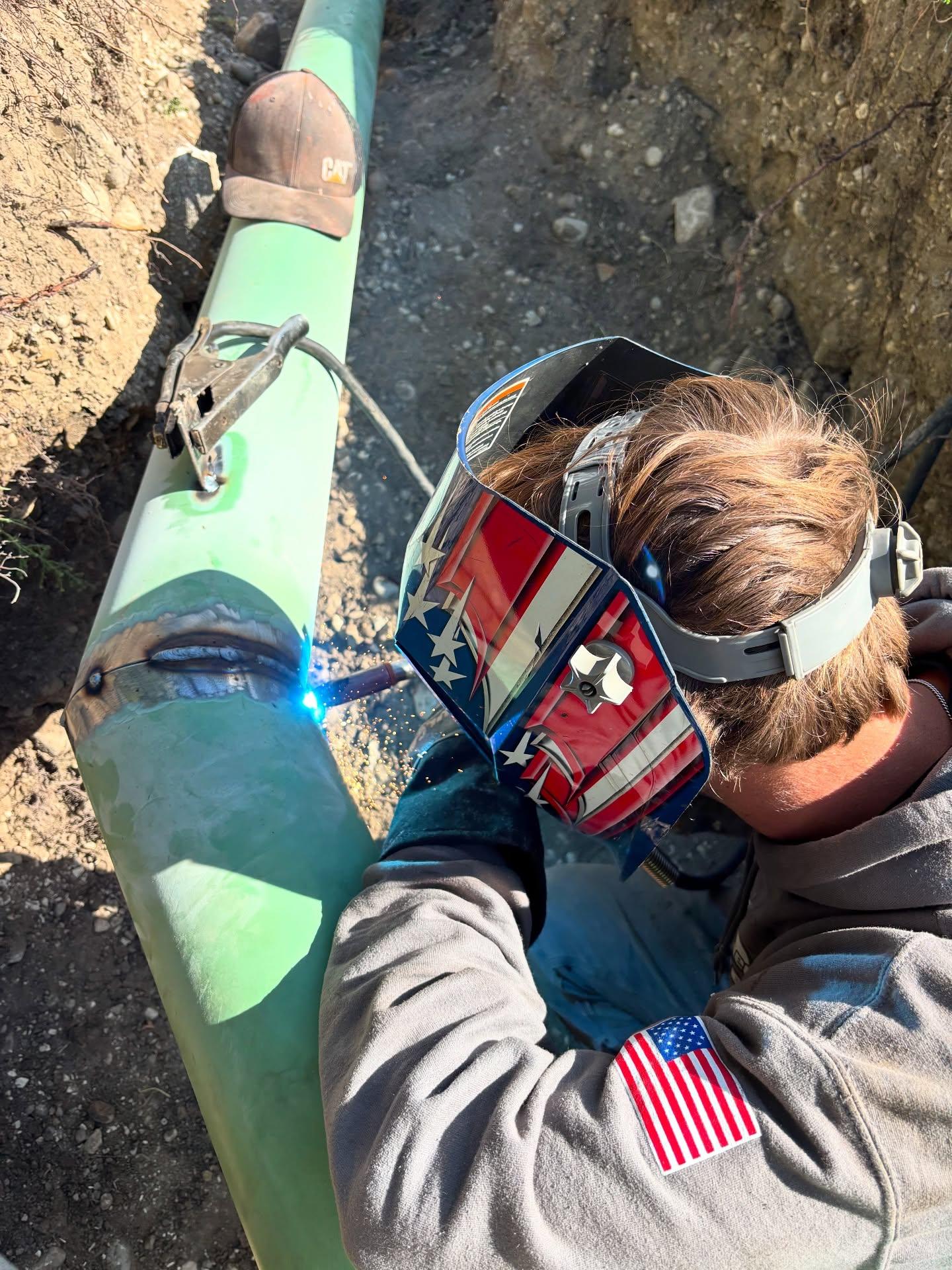 Person wearing protective goggles works beside a green kayak on rocky ground.